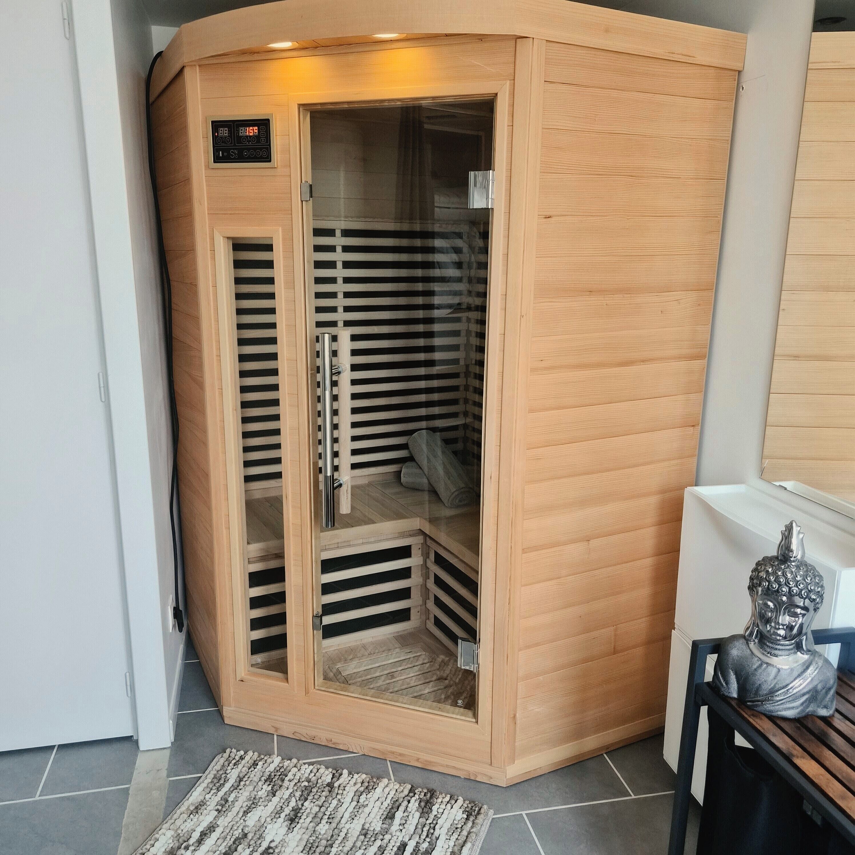 Un sauna d’angle doté d’un écran numérique, d’une porte en verre et d’un intérieur en bois.