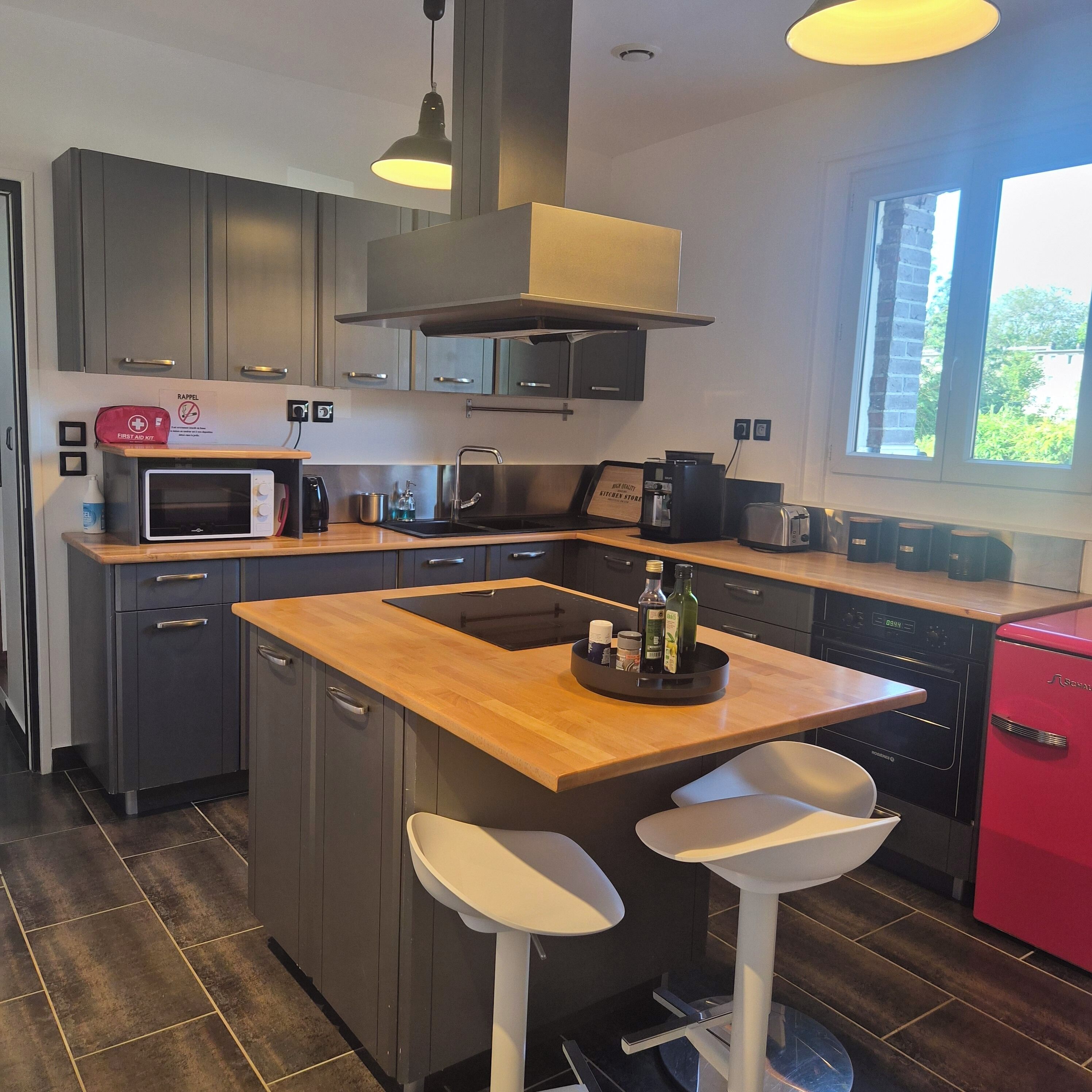 A modern kitchen with a central island, stainless steel appliances, and a red refrigerator.