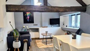 A modern loft with exposed wooden beams, a dining area, a kitchen with a TV, and a living space with a sofa and plants. - Gîte: La Petite Maison de Vernon-Giverny. Wifi, Garden, Free Parking, Giverny (Vernon)