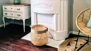 A room with a white fireplace, a mirror above it, a white dresser with drawers, a wicker chair, and a woven basket on the floor. - Gîte: La Petite Maison de Vernon-Giverny. Wifi, Garden, Free Parking, Giverny (Vernon)