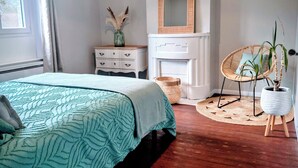 A bedroom with a bed, dresser, mirror, and a wicker chair with a plant. - Gîte: La Petite Maison de Vernon-Giverny. Wifi, Garden, Free Parking, Giverny (Vernon)