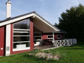 A red building with large windows, a covered patio with chairs, and a white fence. - 4 Star Holiday Home in Grossenbrode (Grossenbrode)