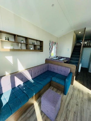 Un salon moderne avec un canapé d’angle, des étagères en bois et un escalier menant à un niveau supérieur.