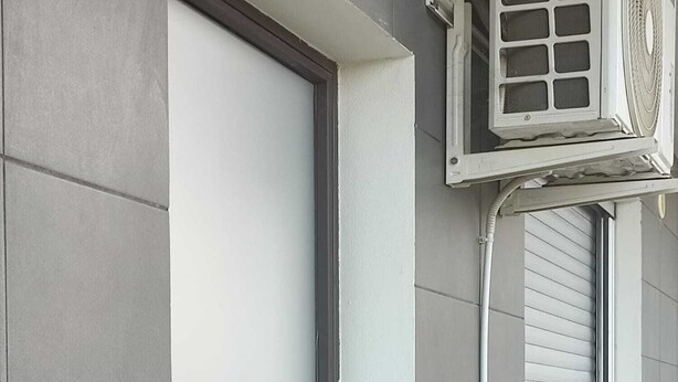 Una puerta con manija, una ventana con persianas y un aire acondicionado instalado en la pared.