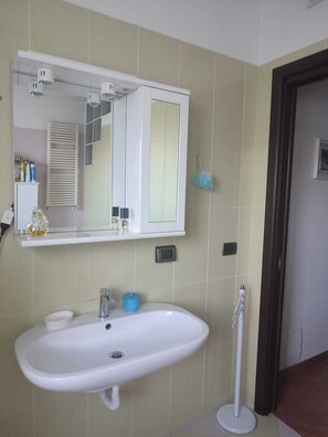 Un baño con lavamanos blanco, un espejo y un perchero para toallas.