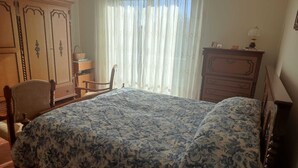 Un dormitorio con cama, una silla, cómoda y ventana con cortinas.