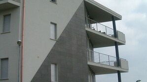 Un edificio de varios pisos con balcones, una tubería de agua visible y un coche en primer plano.