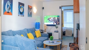 Uma sala de estar com sofá, mesa de centro, televisão e porta que dá para outro cômodo.
