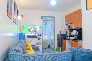 Un espai vital compacte amb un sofà, una televisió, una zona de cuina i una porta corredissa que dóna a un balcó.