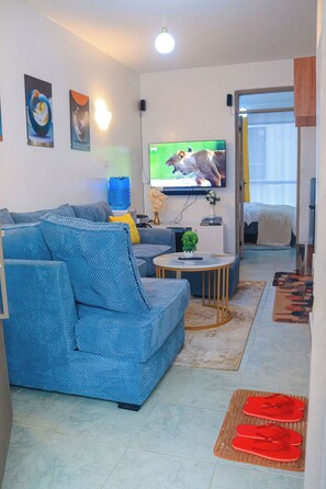 Un saló amb un sofà, una taula de centre, una televisió de pantalla plana i una porta que dona a un altre espai.