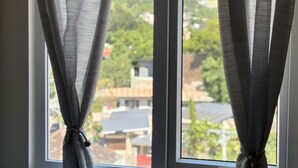 A window with two curtains tied at the top, offering a view of a residential area with houses and greenery. - Urban Oasis Symphony Pool (Cebu City)