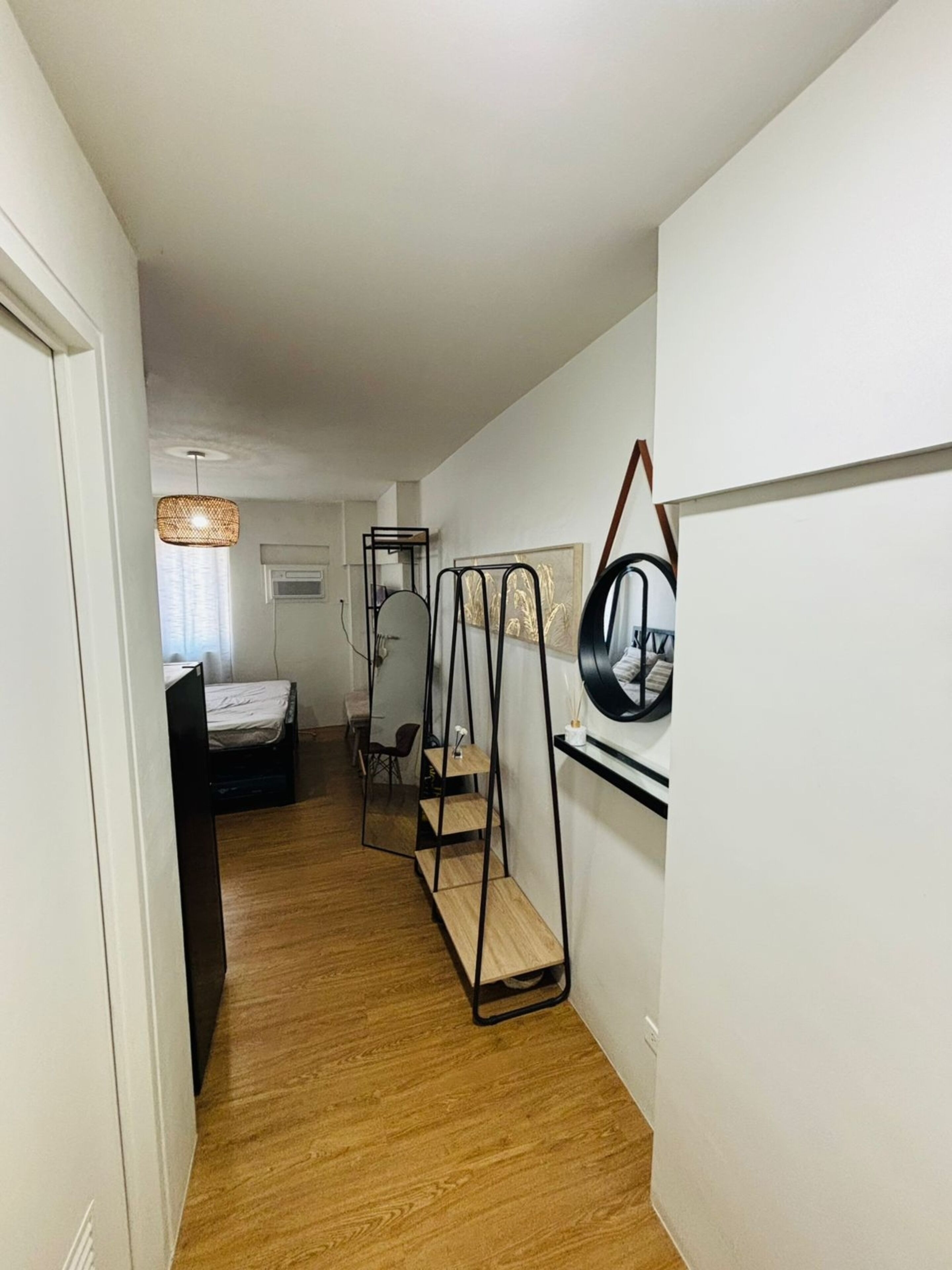 A hallway with a bed, a mirror, and a shelf unit.