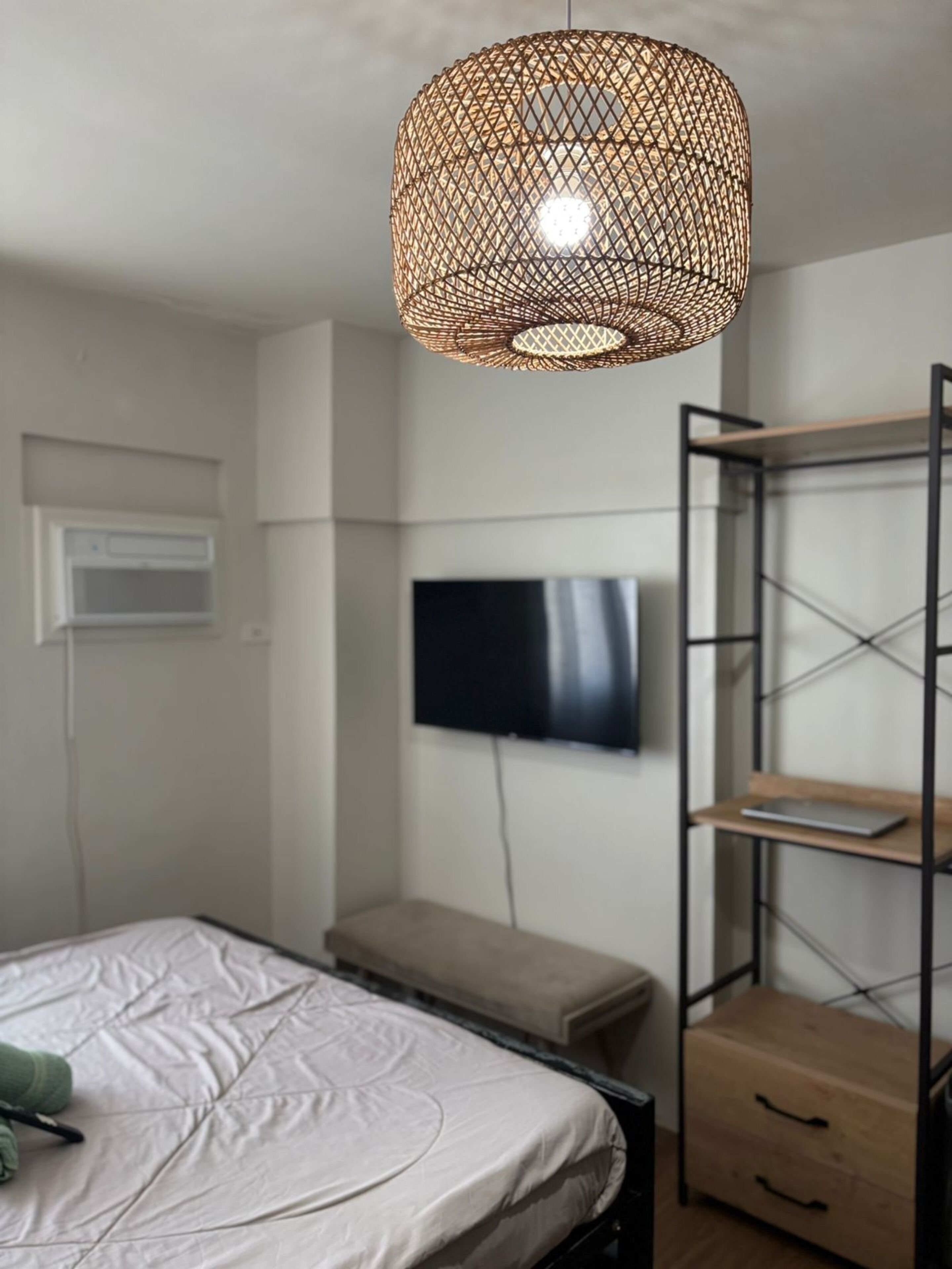 Une chambre à coucher comprenant un lit, un téléviseur fixé au mur, une étagère et un luminaire suspendu.