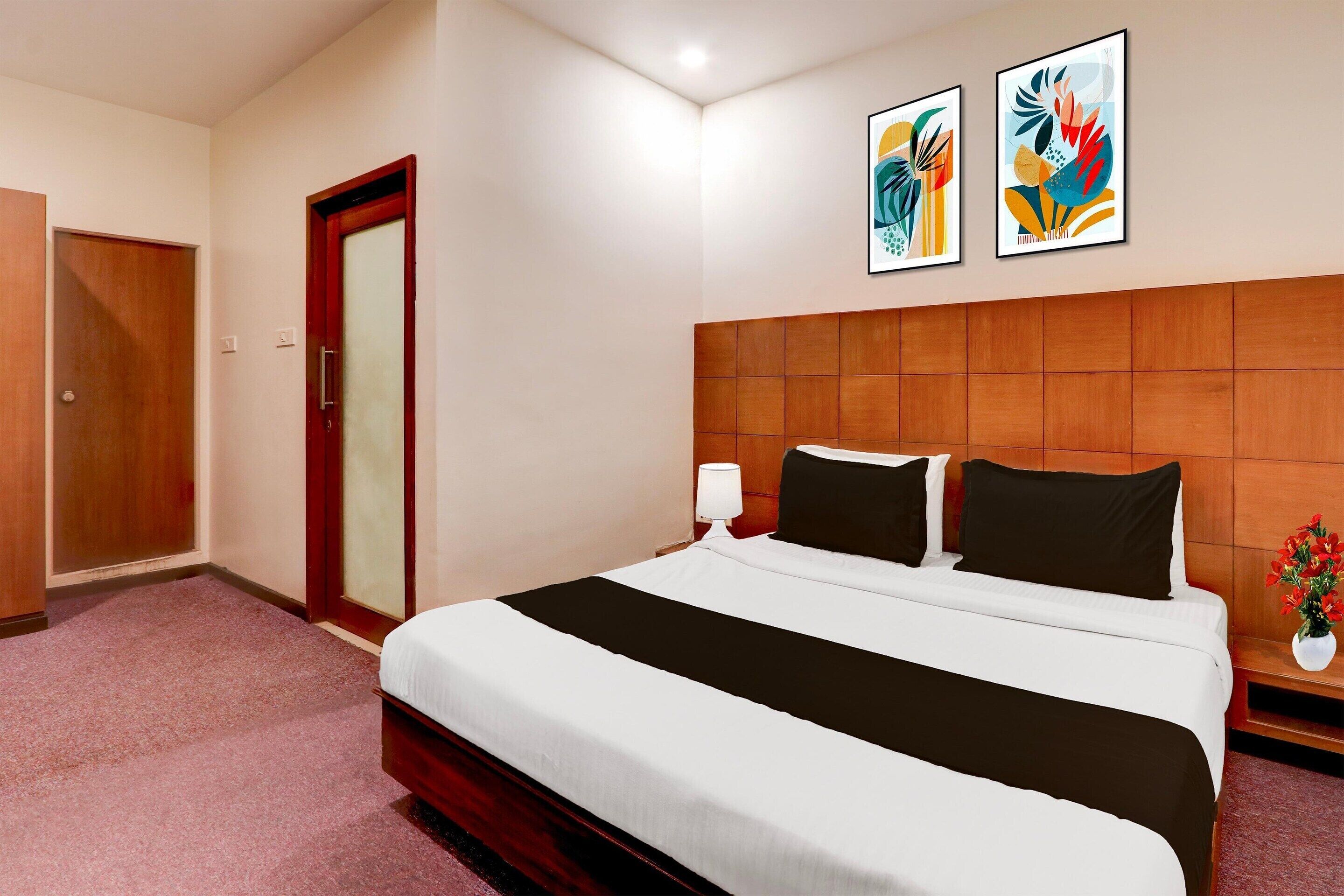 A hotel room with a large bed, a wooden headboard, a door with a frosted glass panel, and two abstract paintings on the wall.