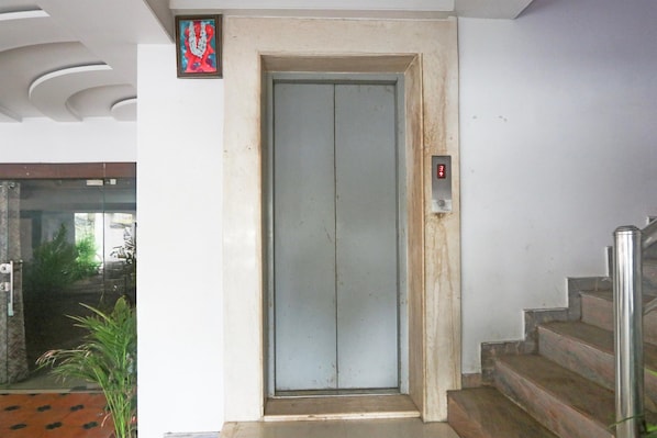 Un ascensor con pantalla digital, una escalera con barandillas de metal y una puerta con un pequeño cuadro enmarcado encima.