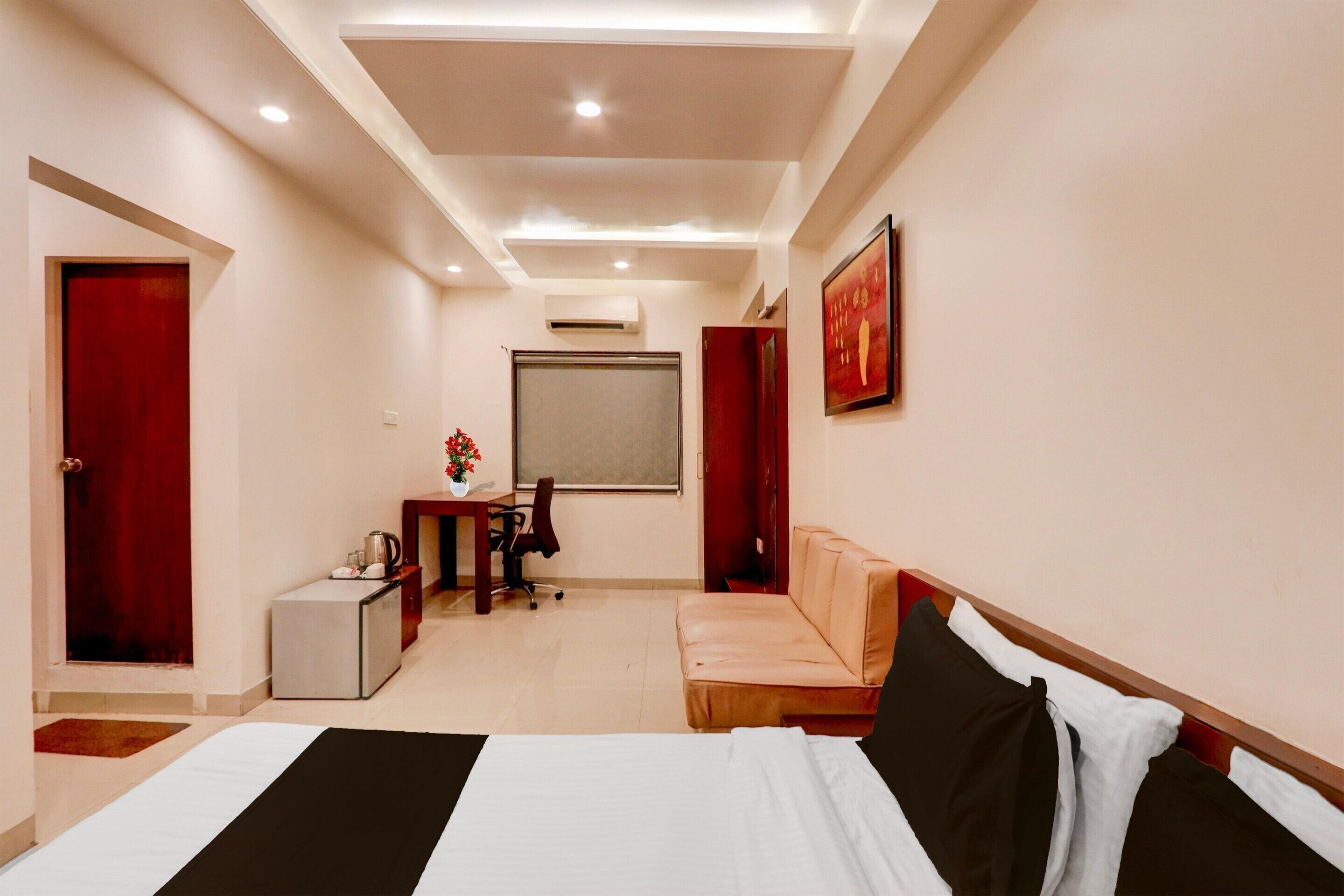 Ein Hotelzimmer mit Bett, Schreibtisch, Stuhl, einem kleinen Tisch mit Blumenvase und einer roten Tür.