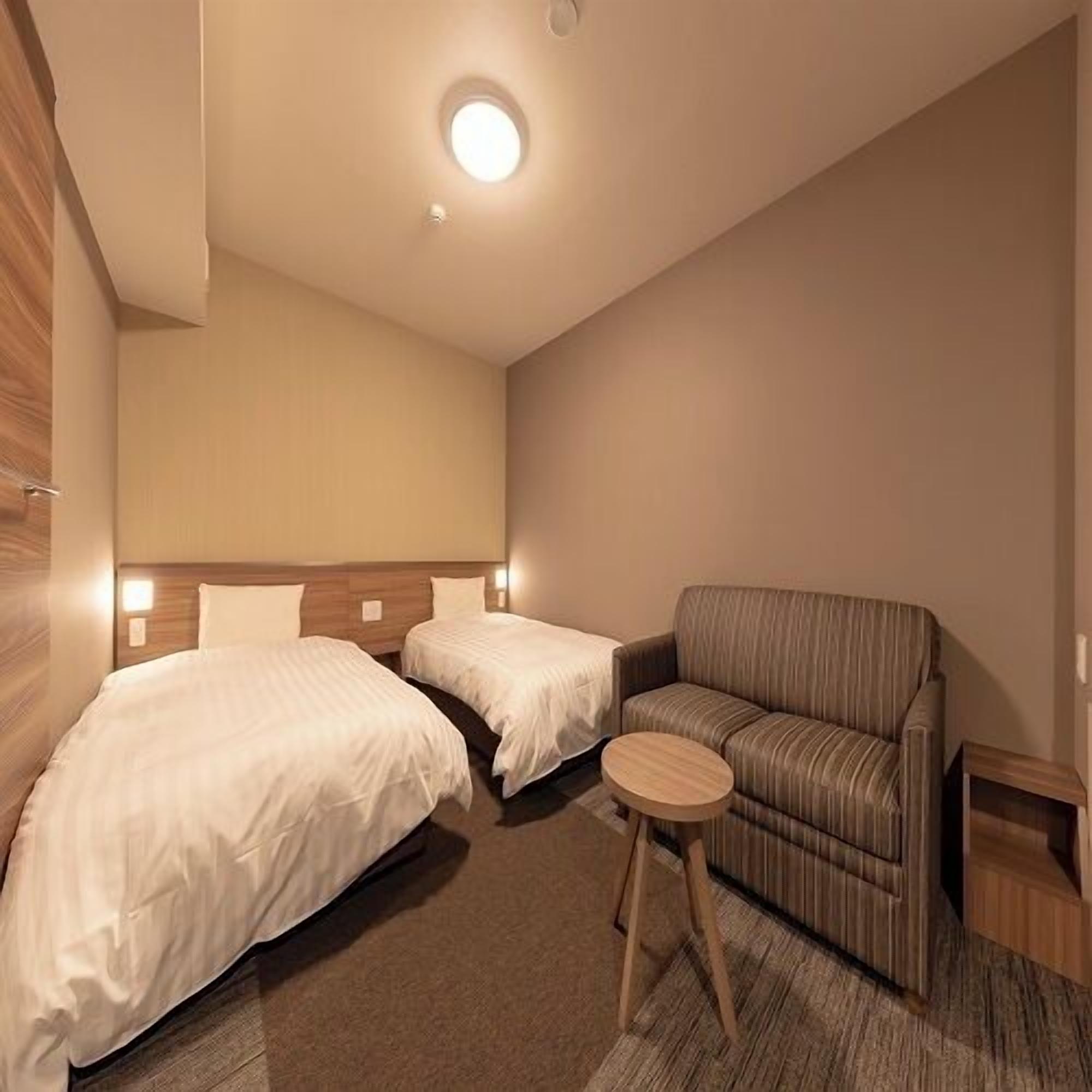 Habitación de hotel con dos camas, un sofá, una mesita redonda y una lámpara de techo.