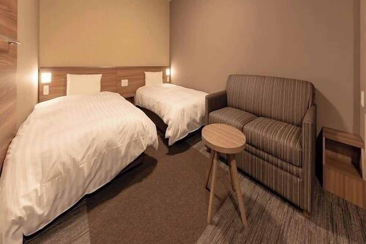 A hotel room with two beds, a sofa, a small round table, and a ceiling light.