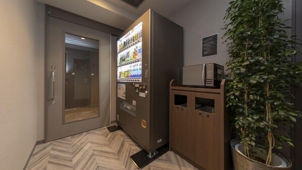 Un distributeur automatique, un four à micro-ondes et une plante en pot dans un couloir.