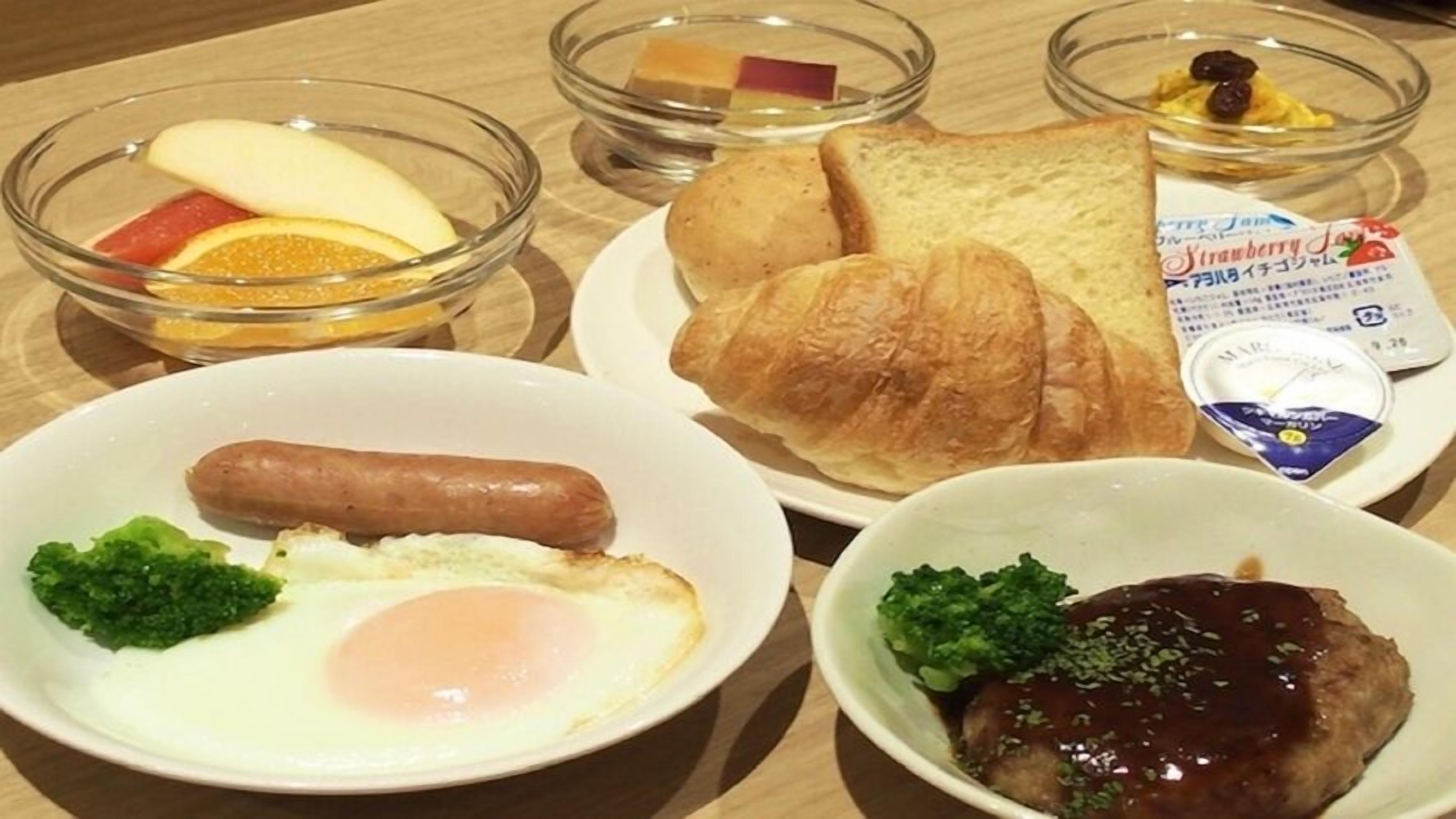 A breakfast setting with croissants, sausage, eggs, and a steak with sauce.