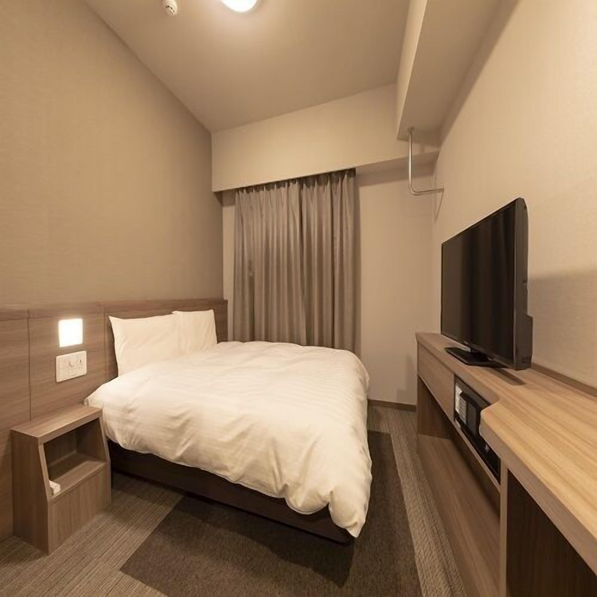 Een moderne hotelkamer met een bed, nachtkastje, televisie en gordijnen.