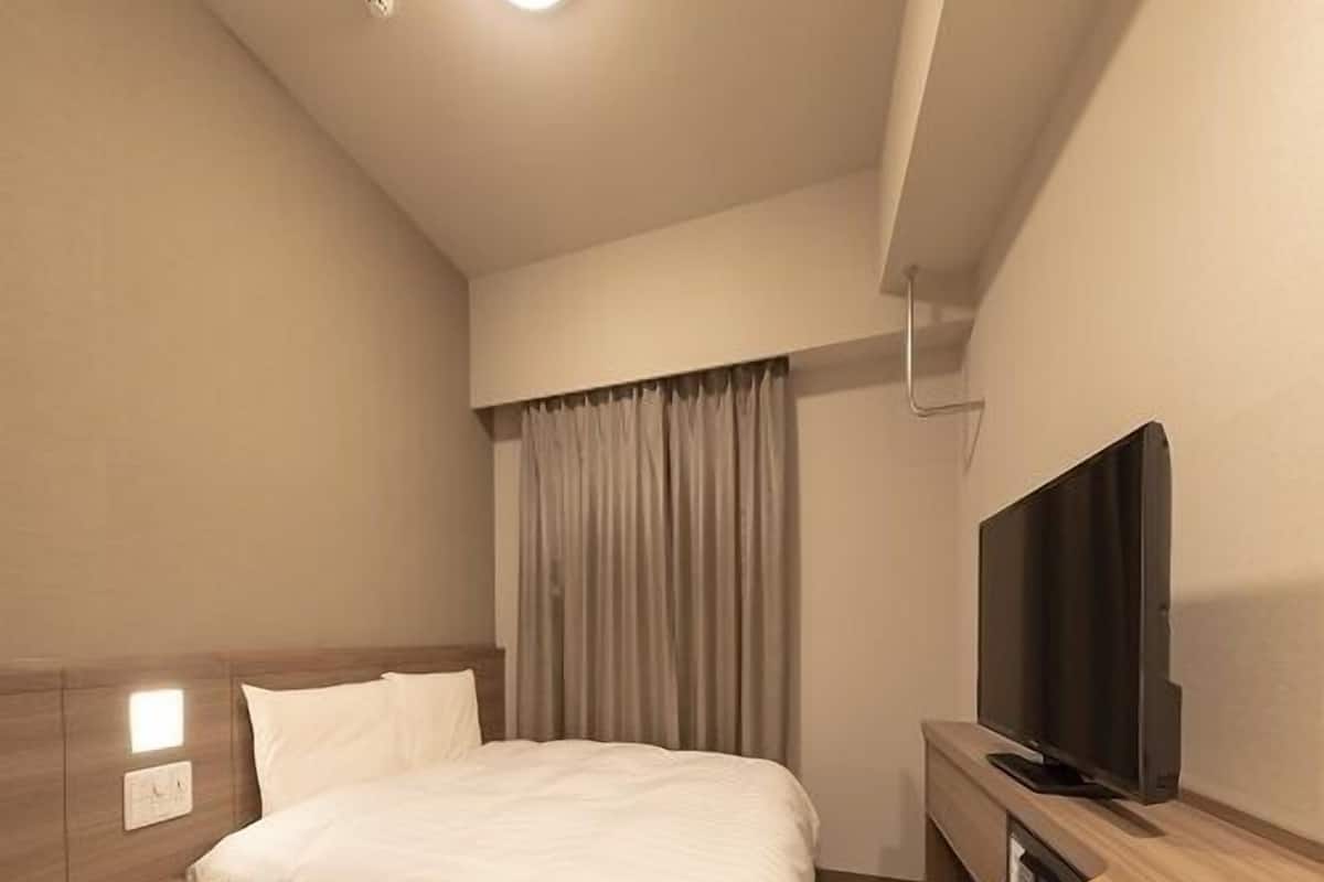 A modern hotel room with a bed, bedside table, TV, and curtains.