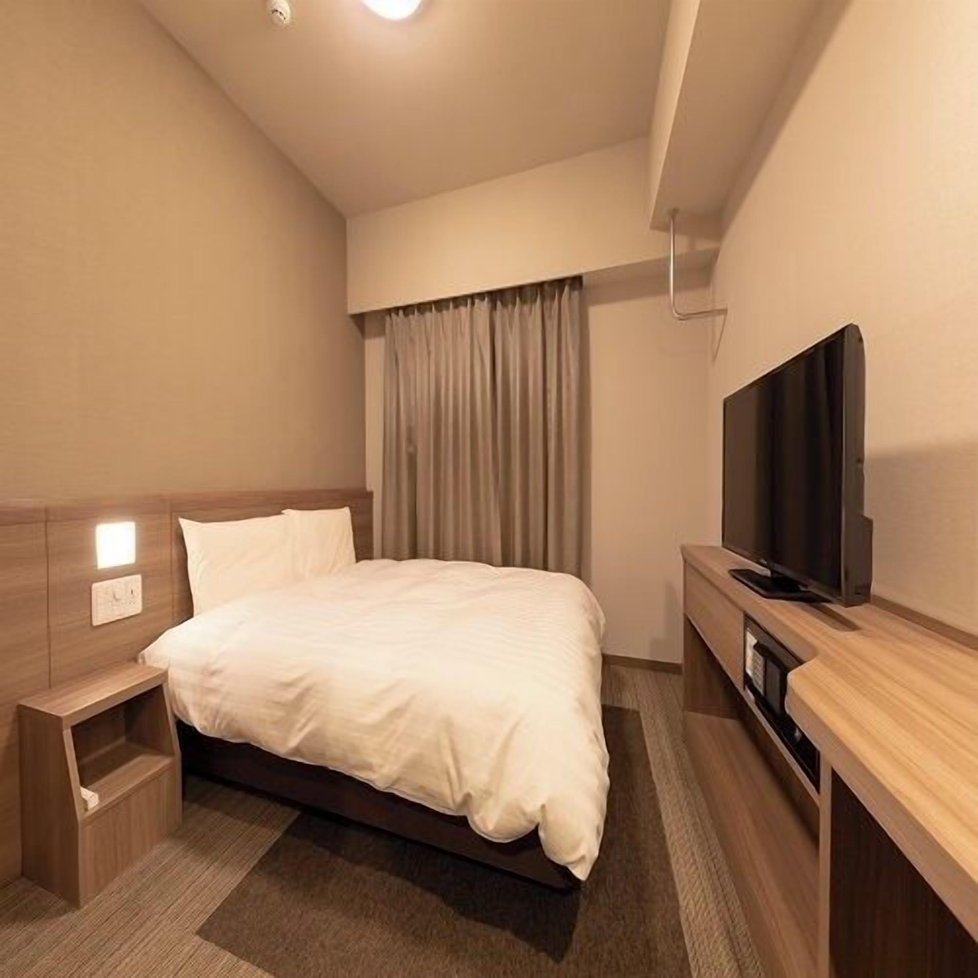 Habitación de hotel con cama, televisión, mesita de noche y ventana con cortinas.
