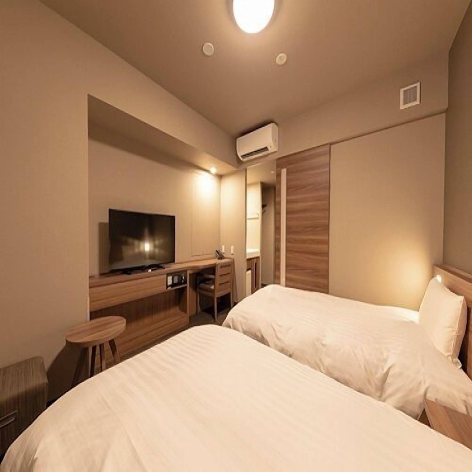 Habitación de hotel con dos camas, televisión, escritorio y aire acondicionado.