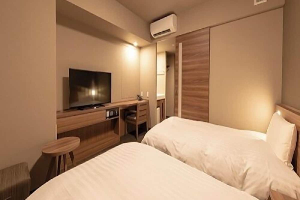 A hotel room with two beds, a TV, a desk, and an air conditioning unit.