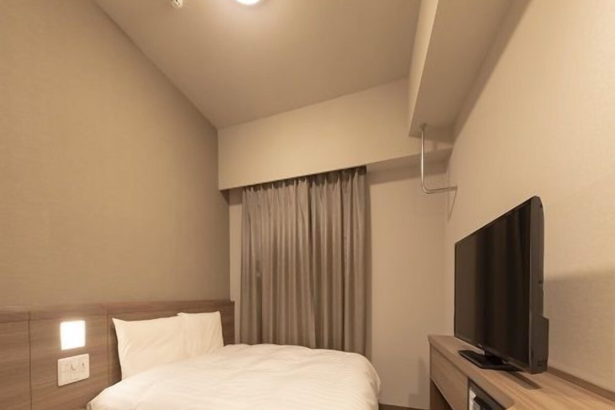 A modern hotel room with a bed, bedside table, TV, and curtains.