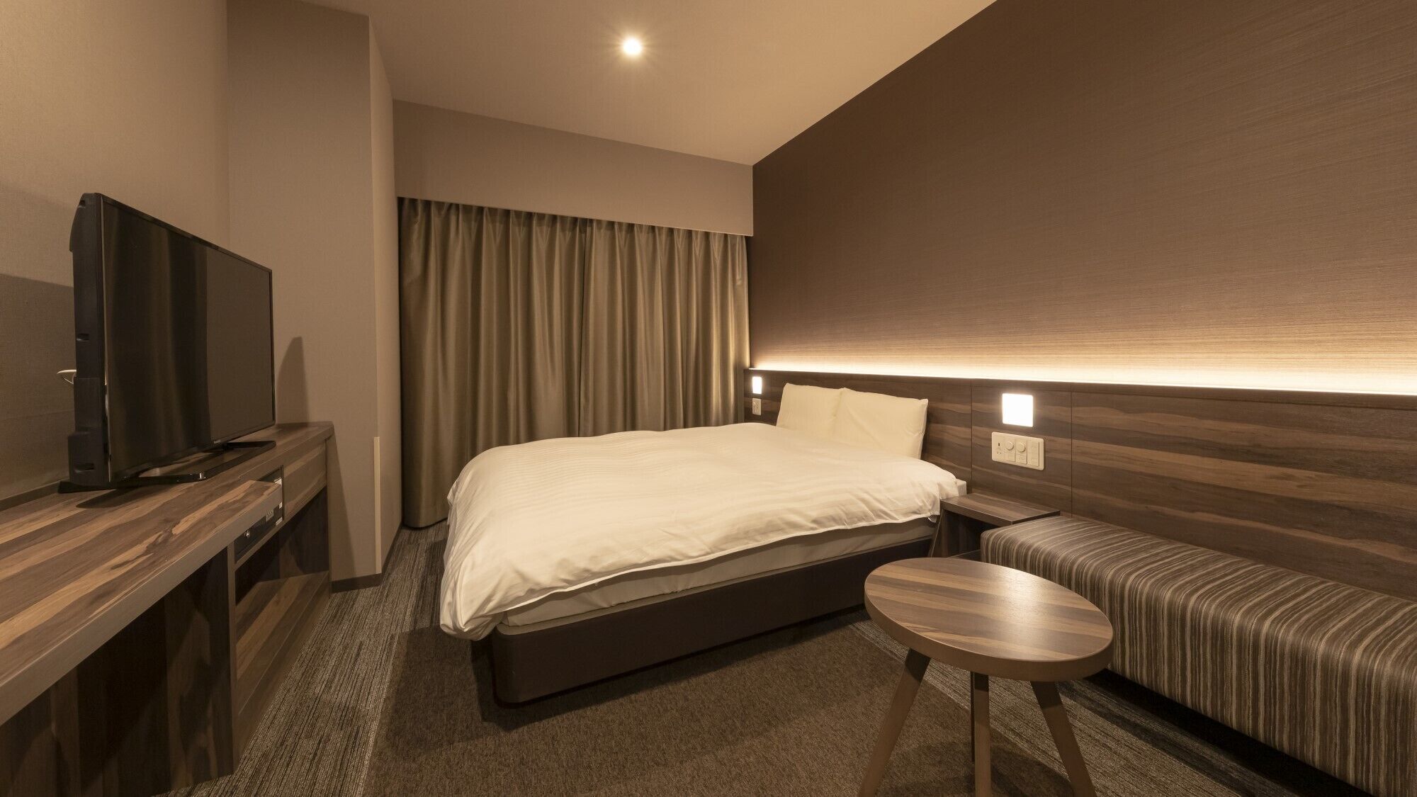 Een hotelkamer met een bed, een televisie, een klein tafeltje en een bank.