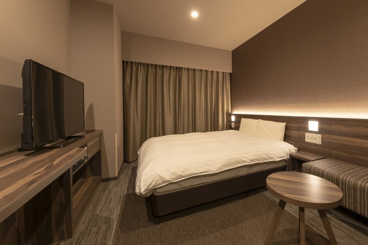 A hotel room with a bed, a television, a small table, and a sofa.