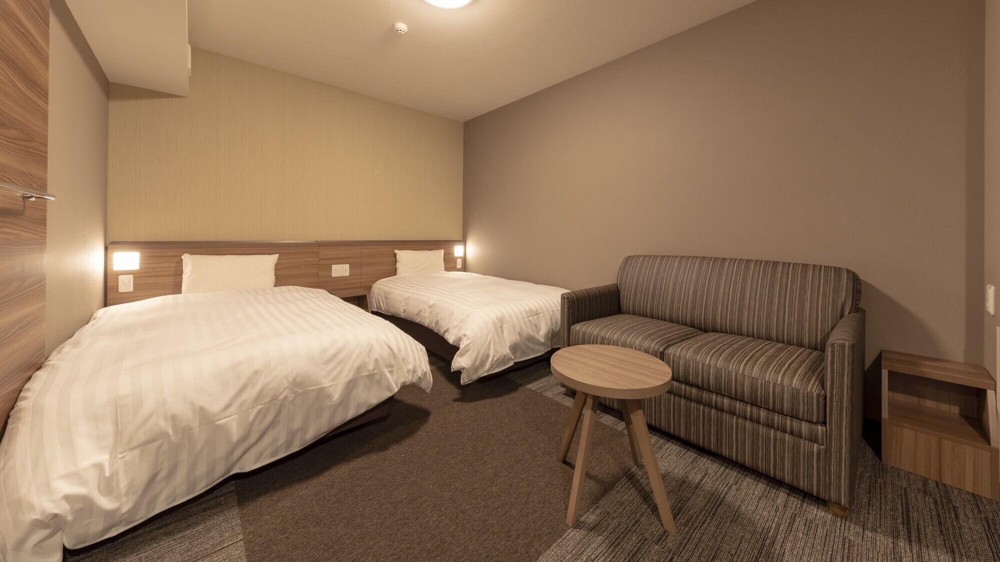 Een hotelkamer met twee bedden, een slaapbank, een klein rond tafeltje en een houten nachtkastje.