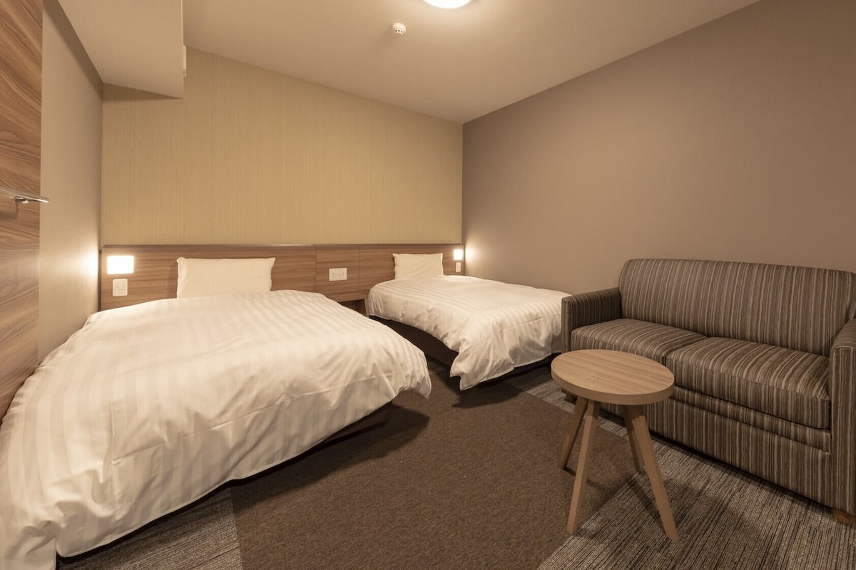 A hotel room with two beds, a sofa, a small round table, and a wooden nightstand.