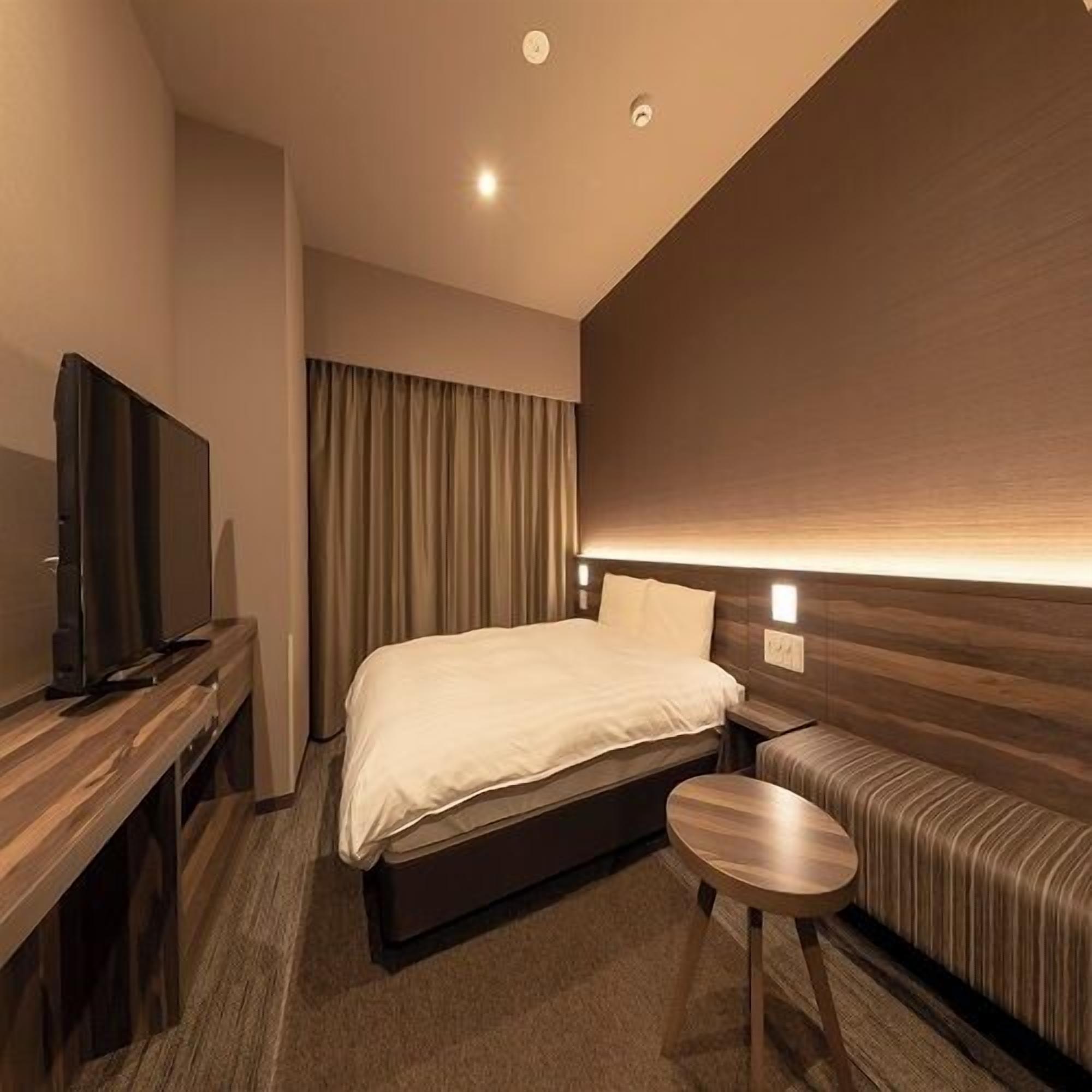 Een hotelkamer met een bed, een televisie op een houten standaard, een klein rond tafeltje en een bank.