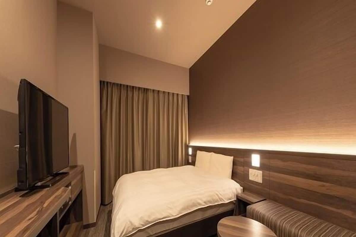 A hotel room with a bed, a TV on a wooden stand, a small round table, and a sofa.