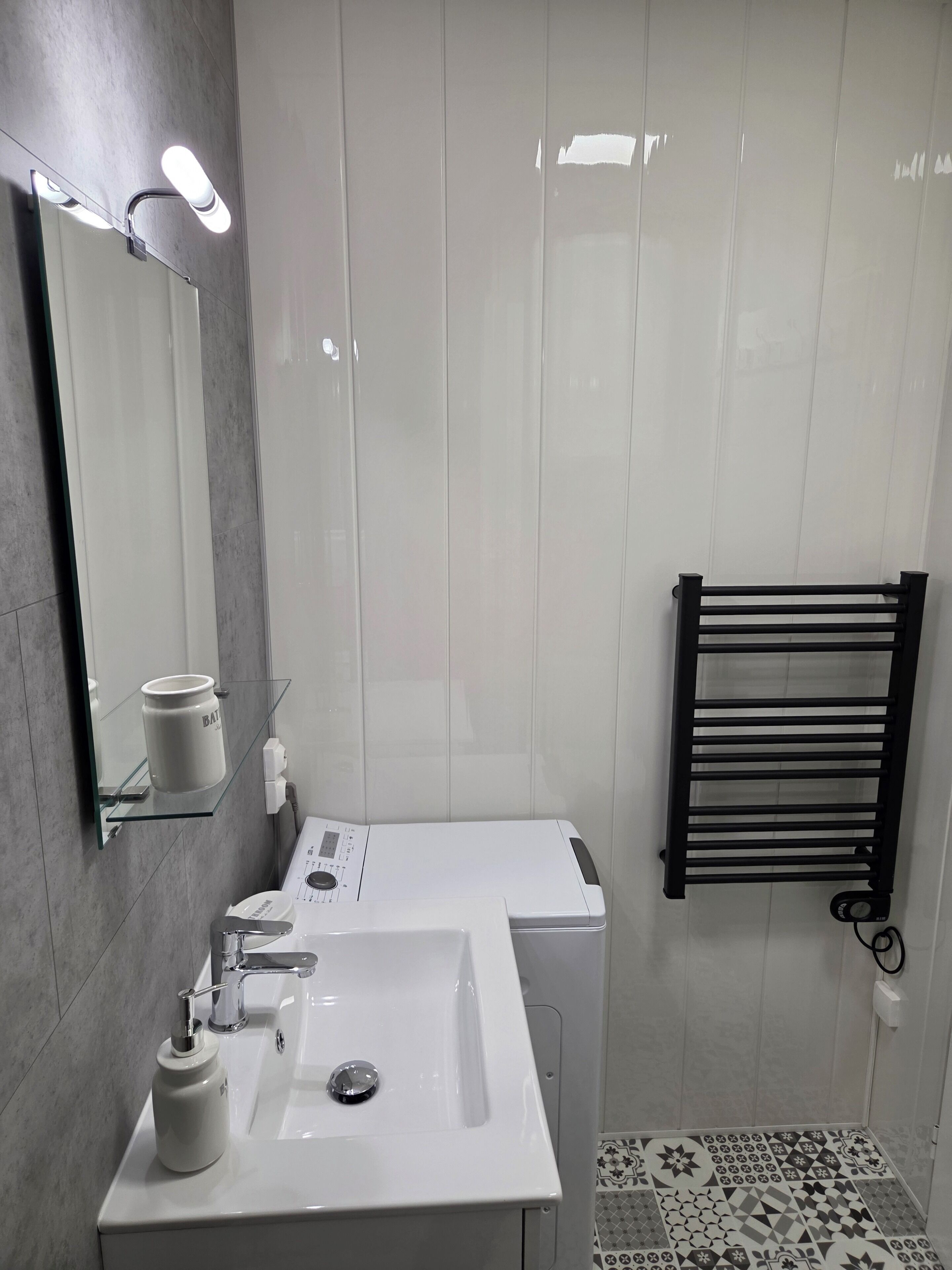 Un baño moderno con un lavabo blanco, un espejo, un perchero para toallas y un suelo estampado.