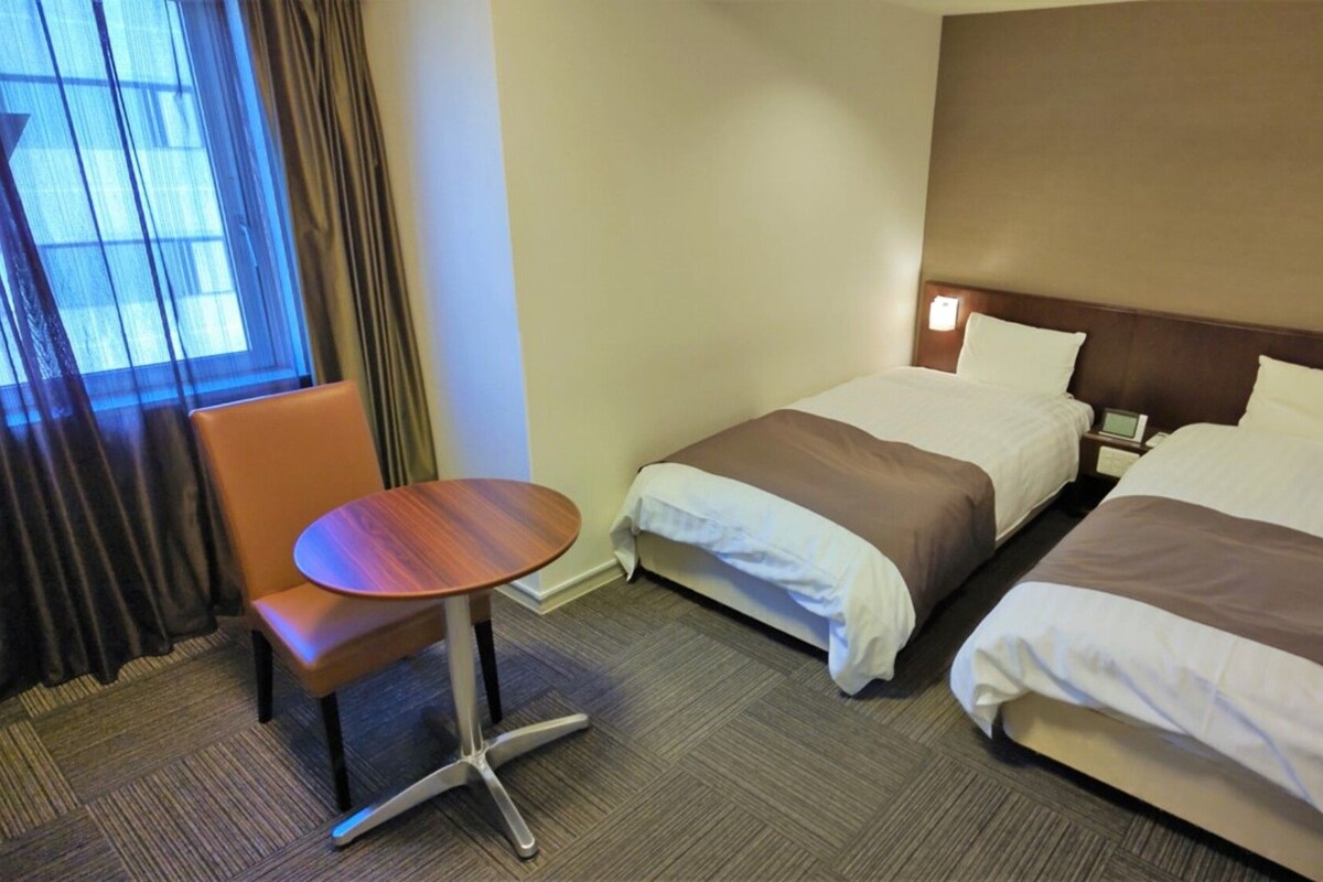 A hotel room with two beds, a small round table, and a chair.