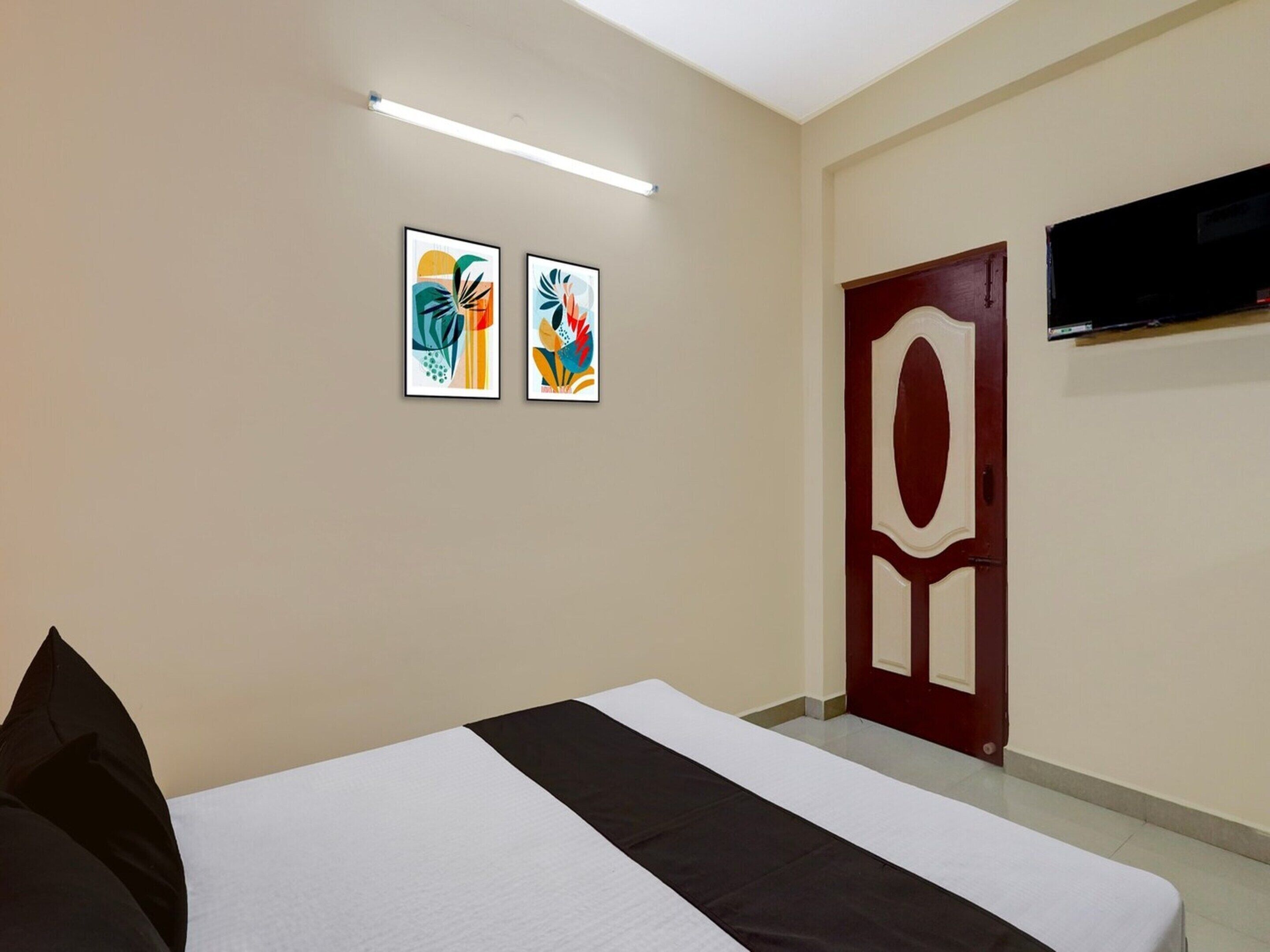 Une chambre d’hôtel avec un lit, deux tableaux abstraits accrochés au mur, un téléviseur fixé au-dessus de la porte et un luminaire au plafond.