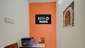 Une chambre d’hôtel avec un mur d’accent orange, un bureau avec une imprimante, une chaise et un panneau indiquant que la chambre est mise à disposition par l’entreprise.