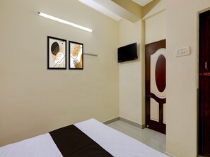 Una habitación de hotel con una cama, un televisor de pantalla plana montado en la pared y dos obras de arte enmarcadas sobre la cama.