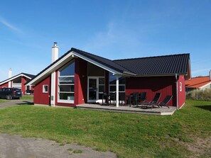 Ein rotes Gebäude mit geneigtem Dach, großen Fenstern und einer überdachten Terrasse mit Sitzgelegenheiten.