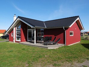 Ein rotes Haus mit einem geneigten Dach, einer Veranda und einer kleinen Terrasse.