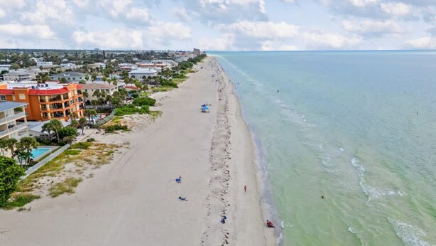 Ein Strand mit einem Hotel auf der linken Seite, blauem Himmel und ruhiger See.