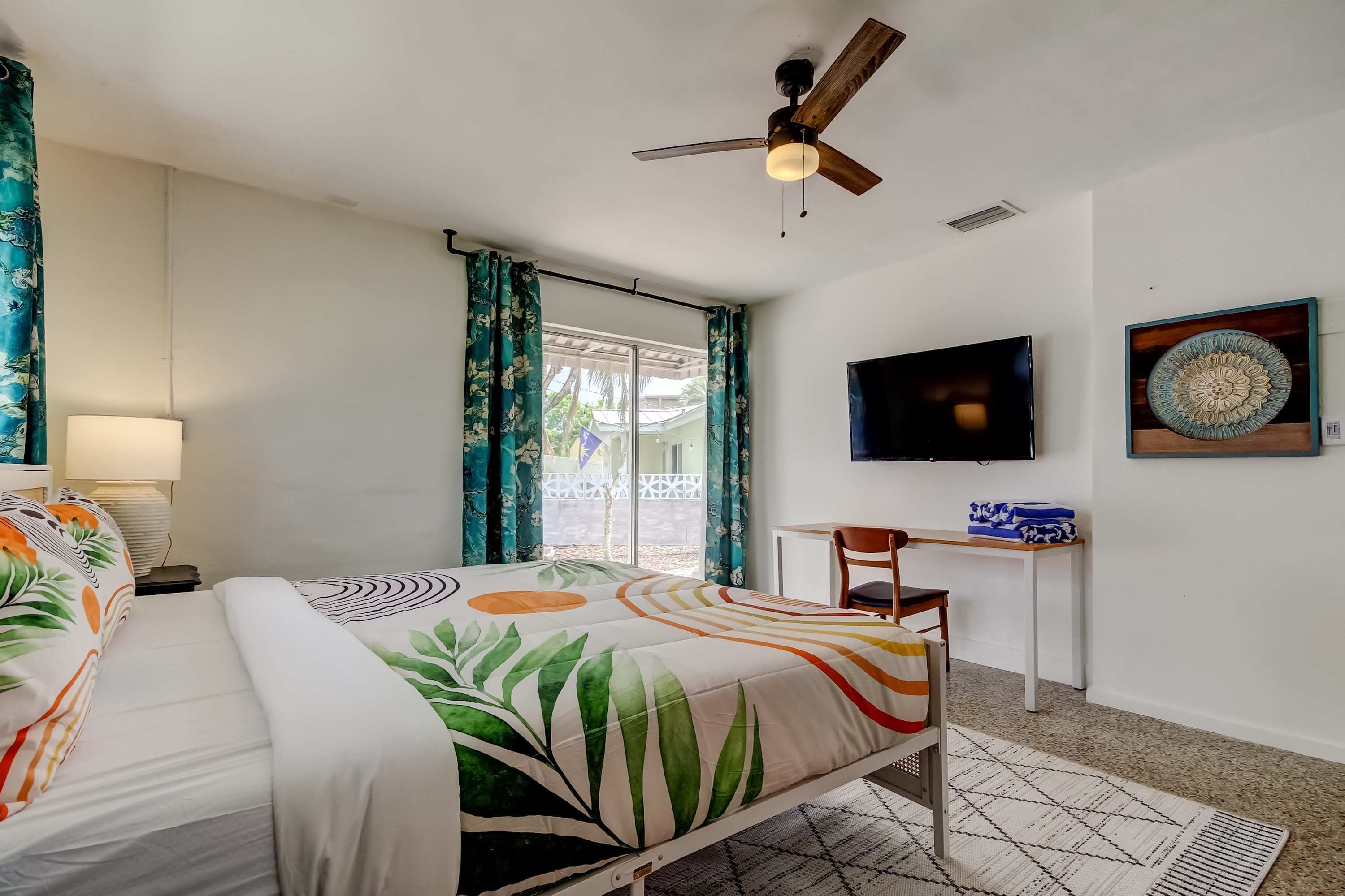 A hotel room with two beds, a ceiling fan, a TV, a desk, and a window with curtains.