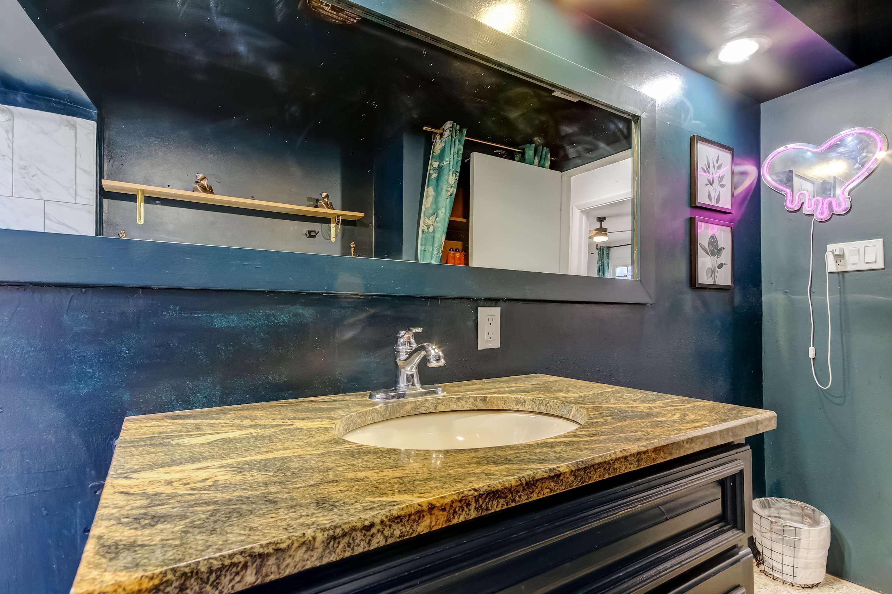 A bathroom with a marble sink, a large mirror, and a neon heart-shaped light.