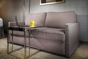 Un canapé gris, avec un ordinateur portable et une tasse jaune posés sur une petite table.