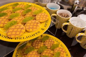 A table with plates of waffles and green sugar decorations, surrounded by patterned cups and bowls.