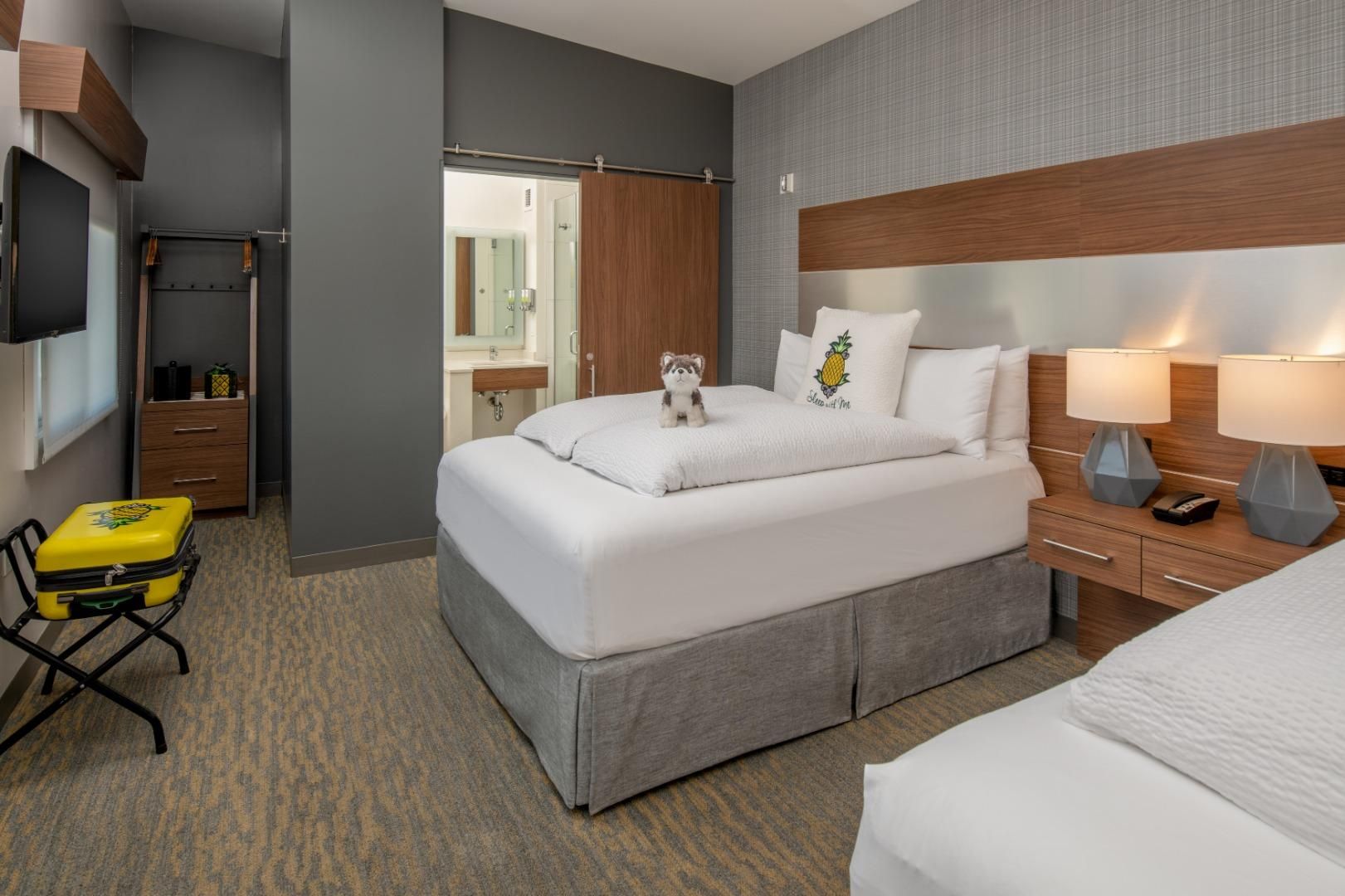 Habitación de hotel con cama, mesita de noche, lámpara y maleta sobre una silla.