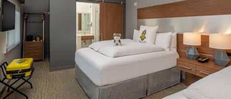 Habitación de hotel con cama, mesita de noche, lámpara y maleta sobre una silla.